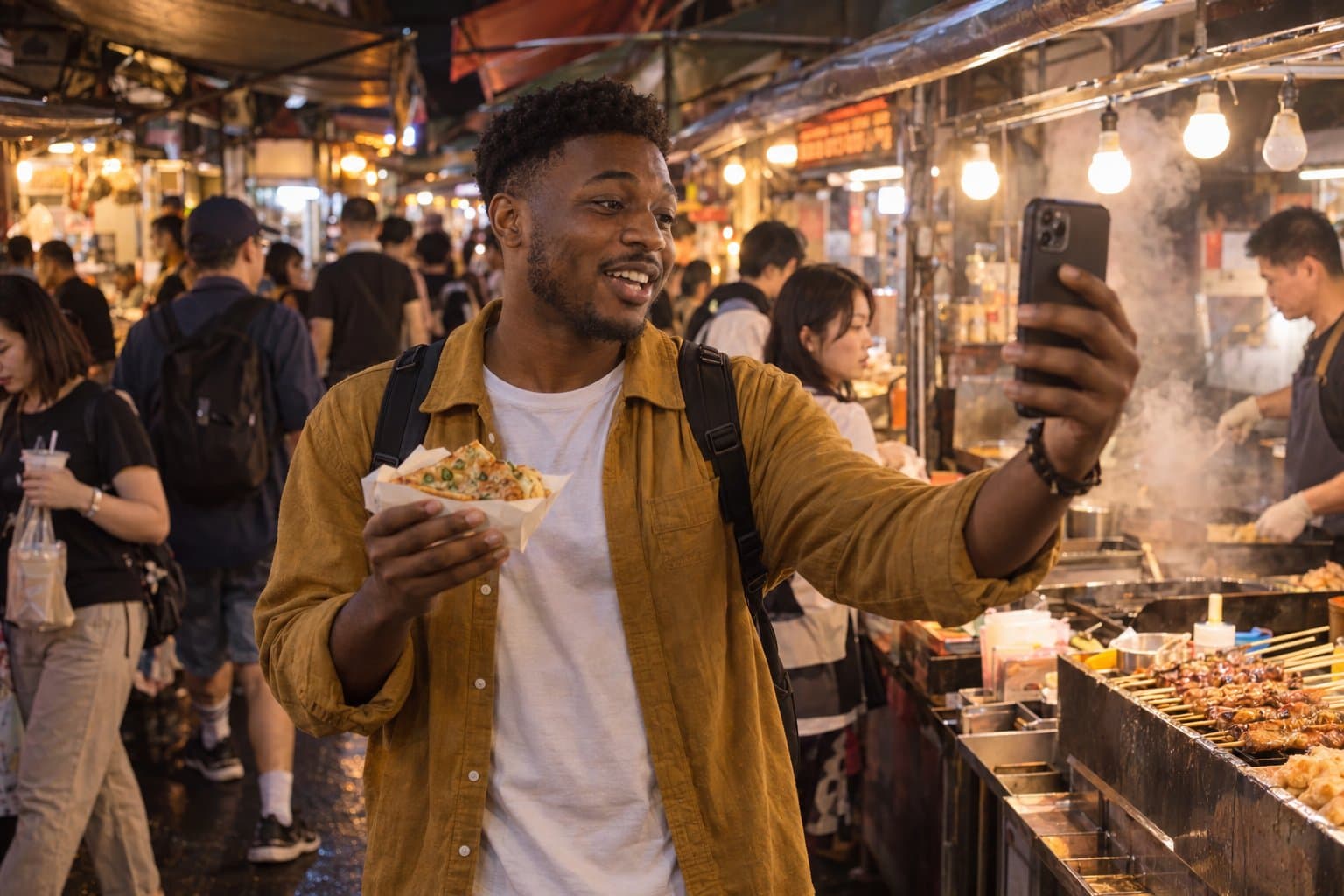A young traveler films a selfie video on his phone at a busy night market, holding a paper tray of street food